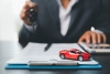 Person holding car keys in front of a clipboard with a toy car