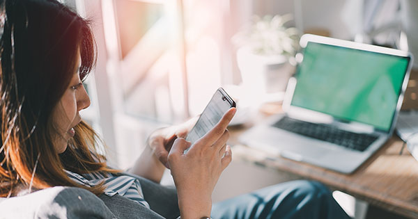 Woman using cellphone and sitting by open laptop