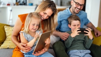 Family of 4 smiling while using a phone and tablet