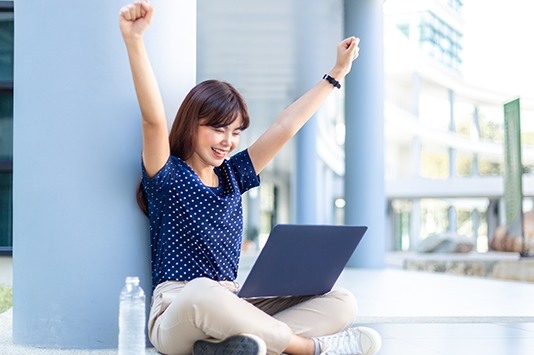 Happy young woman feeling accomplished at laptop