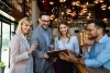 Four business professionals out at a restaurant looking at a tablet together and smiling