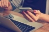 A closeup of a woman with pink nails holding her phone while also on her laptop.
