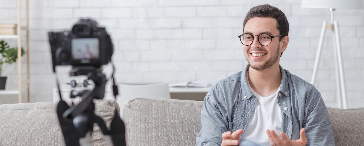 Smiling man sitting in front of a camera on a tripod