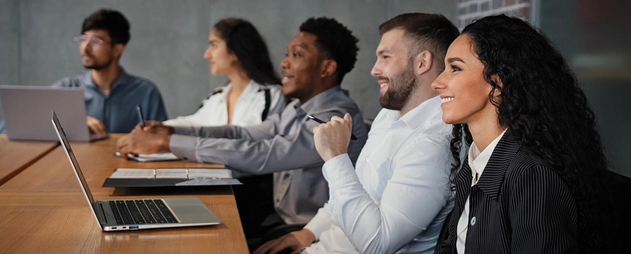 Smiling professionals sitting with laptops at a conference room table