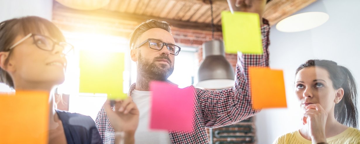 3 people developing a plan with colorful sticky notes on a clear board.