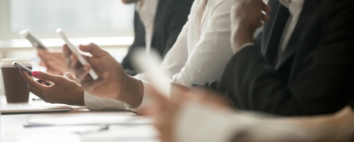 Photo of a group of office workers at a conference room table using their mobile phones