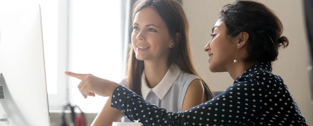 Photo of 2 business professionals having a discussion while one of them points at a computer monitor