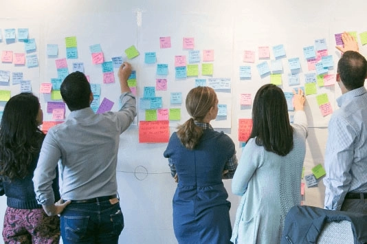A group of people collaborating at a whiteboard, brainstorming and organizing ideas, illustrating the collaborative nature of Agile development in refining and prioritizing tasks.