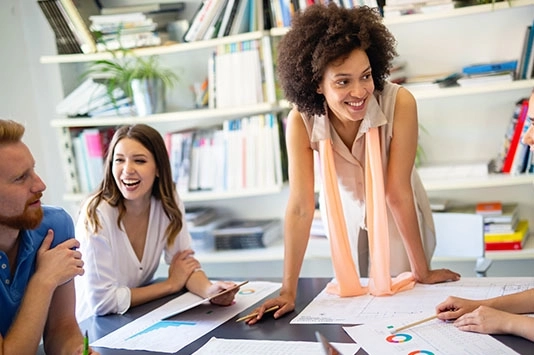 Happy coworkers collaborating at a desk, smiling as they review and align on acceptance criteria, highlighting the positive teamwork involved in refining project goals.