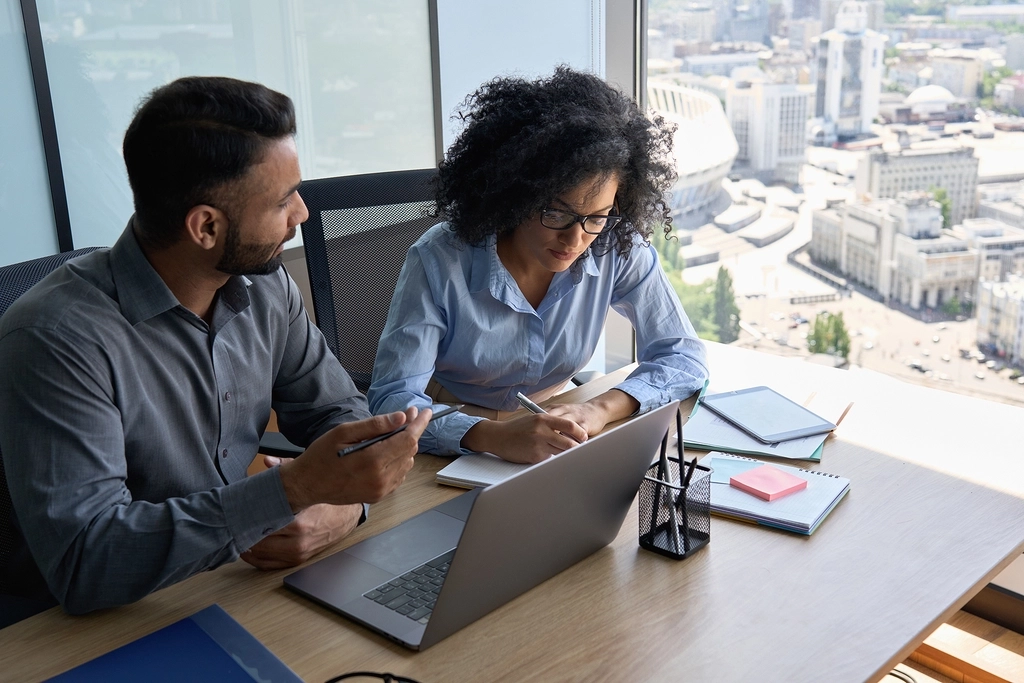 Two coworkers collaborating closely at a desk, discussing and refining a user story, demonstrating teamwork in the Agile development process.