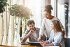 3 coworkers huddled around a desk pointing to a tablet