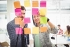 Two designers reviewing sticky notes on a glass board. 