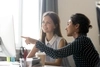Photo of 2 business professionals having a discussion while one of them points at a computer monitor