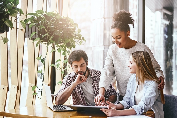 3 coworkers huddled around a desk pointing to a tablet