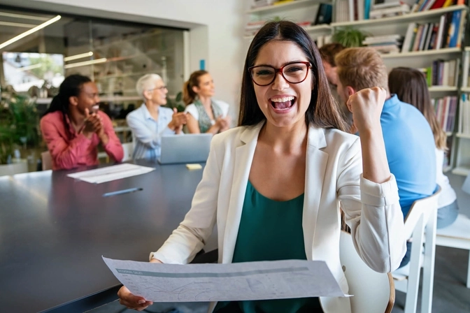 Smiling woman celebrating with raised fist with smiling colleagues in the background
