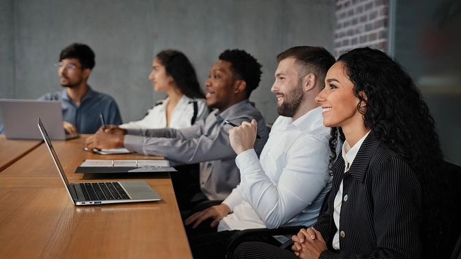 Smiling professionals sitting with laptops at a conference room table