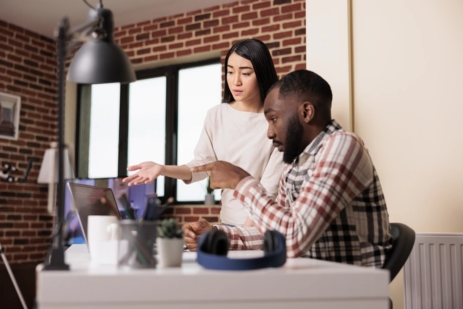Photo of a man and a woman at a desk pointing at a computer screen having a discussion