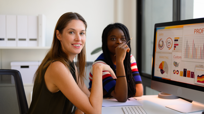 hypotheses user research Photo of two women sitting at a desk looking at monitor showing a dashboard of ecommerce metrics