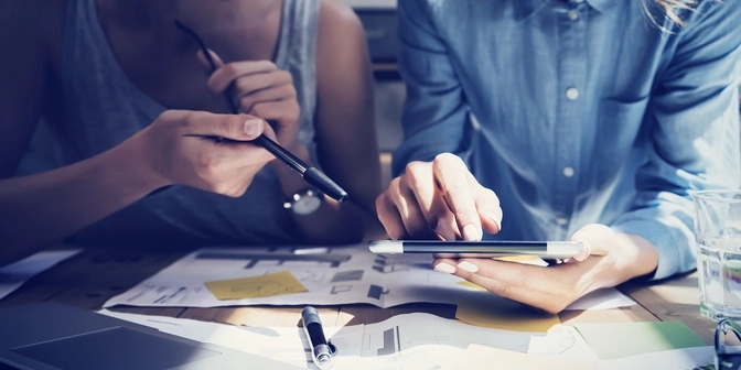 Photo of 3 people at a conference table looking at a tablet