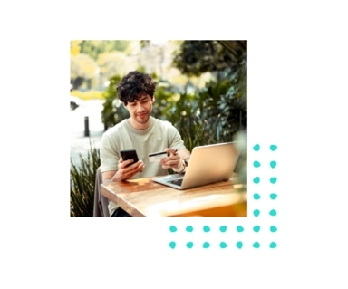 Photo of a person sitting outside while looking at their cell phone and holding their credit card