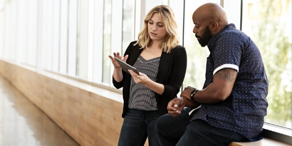 Image of man and woman in a hallway talking and looking at a tablet in the workplace