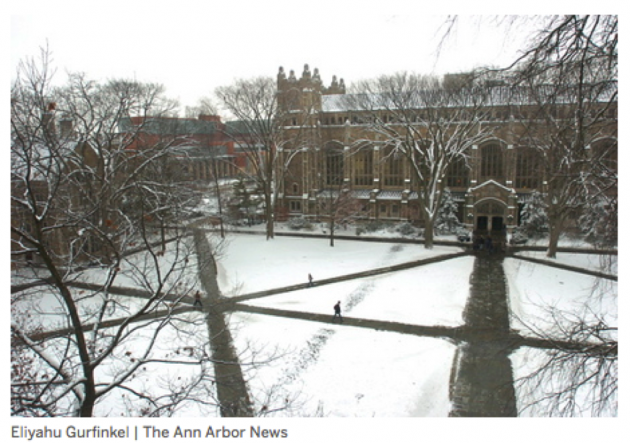 Person walking on a university campus through snow, parallel to a sidewalk